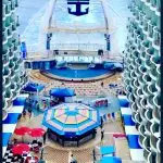 View of a cruise ship's vibrant central atrium, featuring a stage, seating areas, and colorful umbrellas, showcasing leisure activities onboard.