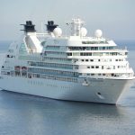 A large luxurious cruise ship sails through calm waters, showcasing multiple decks and amenities designed for passenger comfort and leisure.