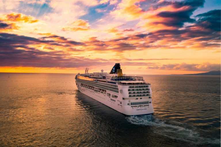 A cruise ship sails through calm waters under a vibrant sunset sky, highlighting travel and adventure on the open sea.
