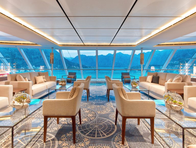Sleek lounge with plush seating and expansive windows showcasing mountains and water, offering a luxurious ambiance for relaxation and views.