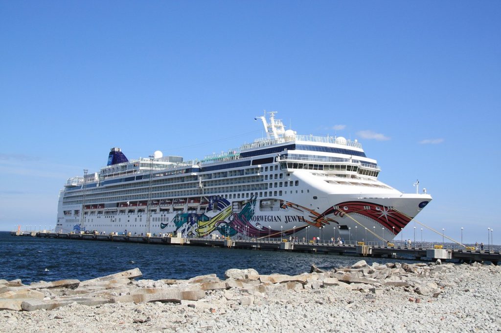 Norwegian Jewel cruise ship docked at a pier, showcasing its vibrant hull artwork against a clear blue sky. Ideal for travel promotions.