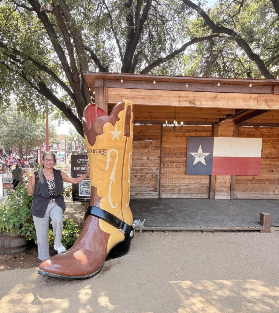 Woman standing next to a big texas boot and flag of texas