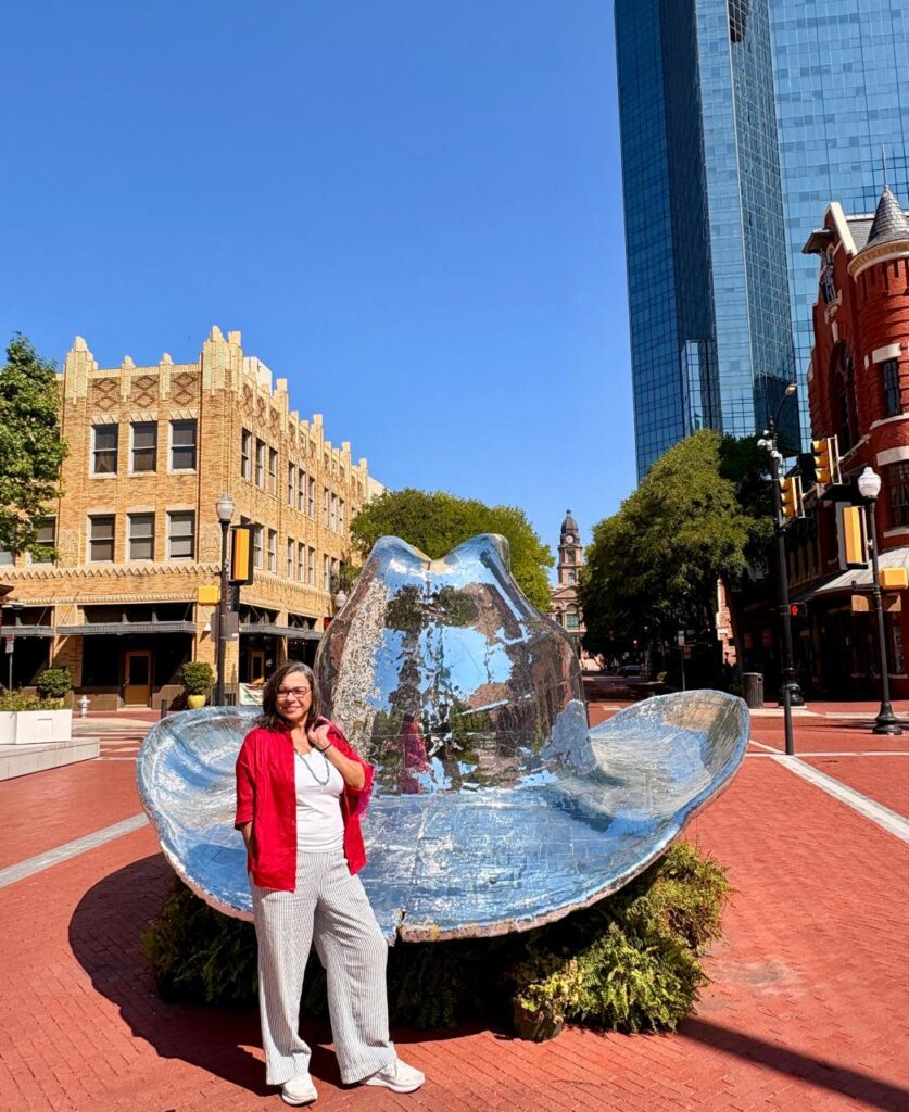 a woman standing in front of a silver oversized cowboy hat